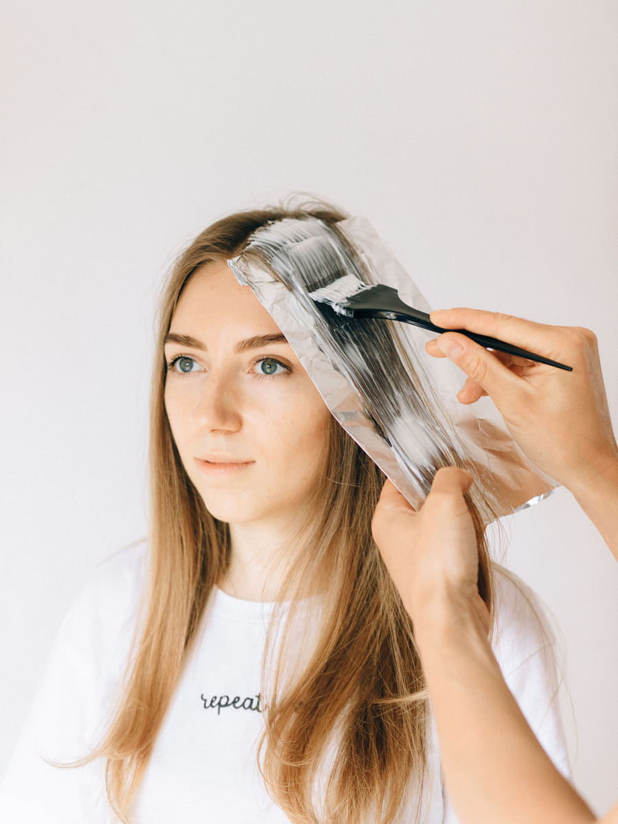 A woven section of hair being painted with lightener and folded into foil, the placement that separates highlights from freehand balayage.