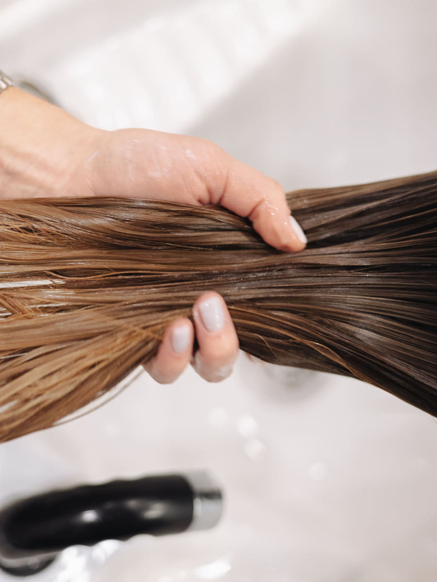 A hand working shampoo through a section of wet hair at the shampoo station, L’Amour Luxe Salon in Sector 20, Kharghar.