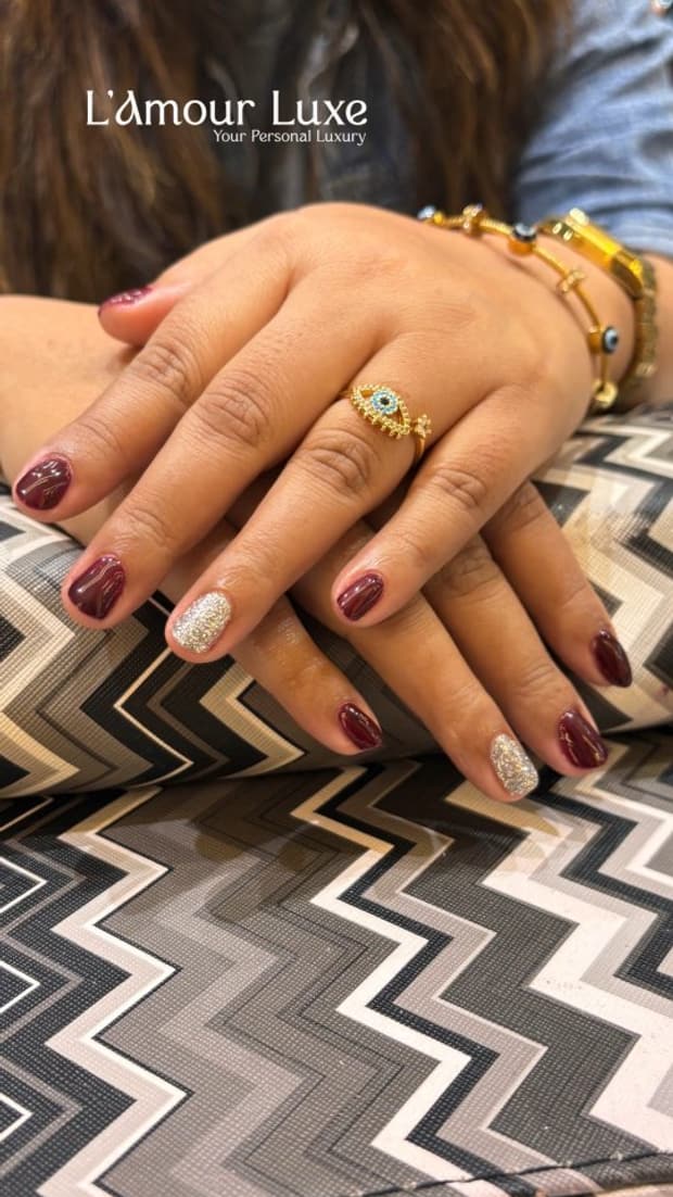Two hands resting on a patterned surface, nails finished in deep maroon with cream and gold accent art.
