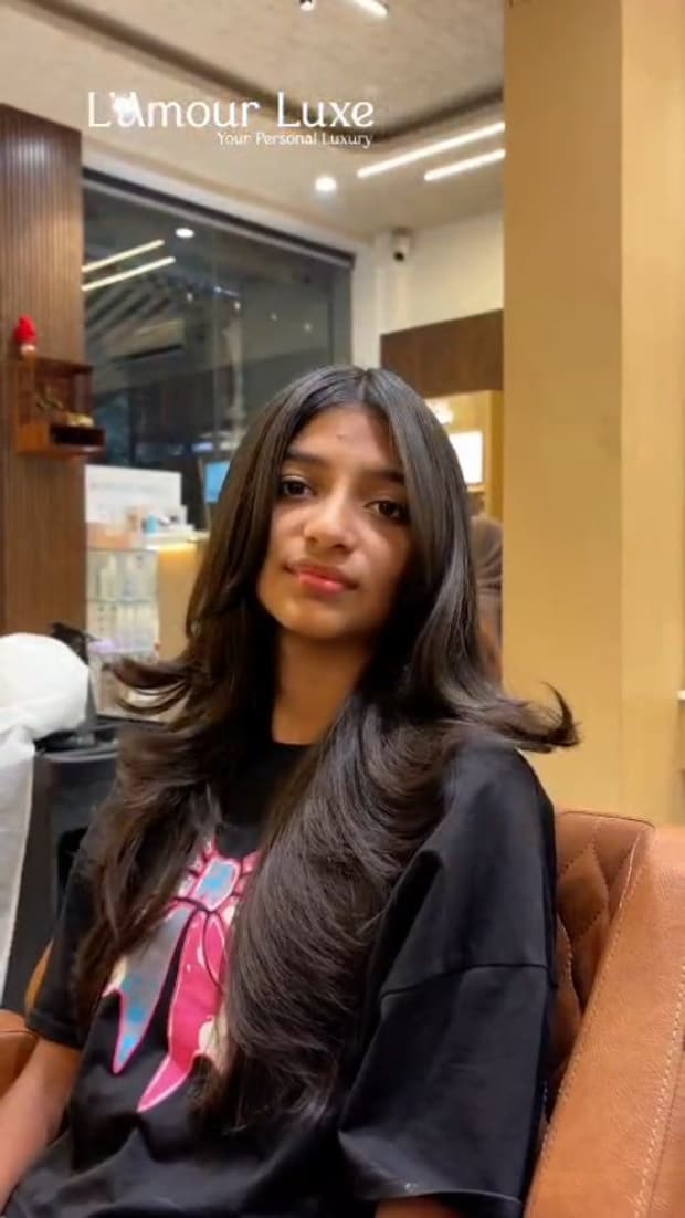 A client seated in the salon, long dark hair blow-dried into soft face-framing layers.