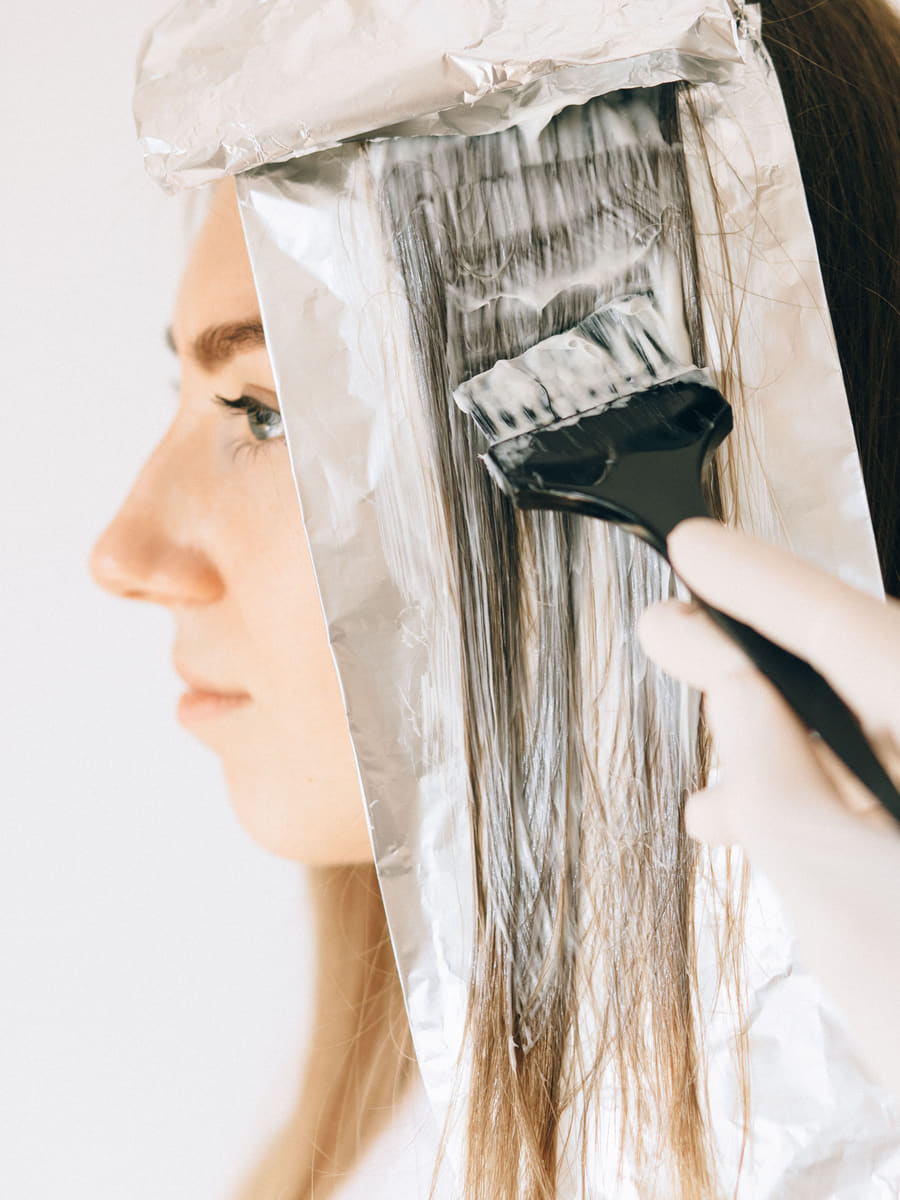Colour being brushed onto a held section of hair laid on foil, the client in profile behind it.