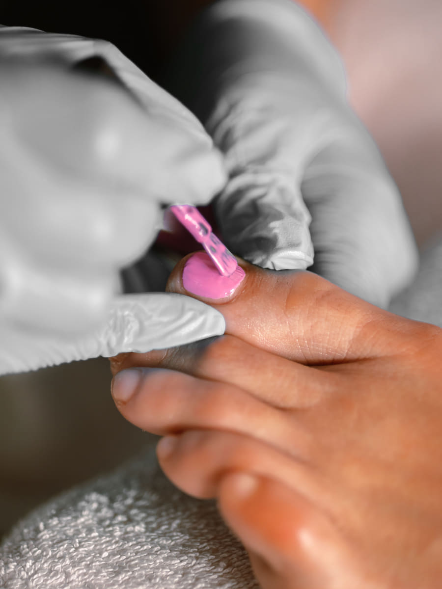 A close view of polish being applied to a toenail during a pedicure, the technician working in gloves.