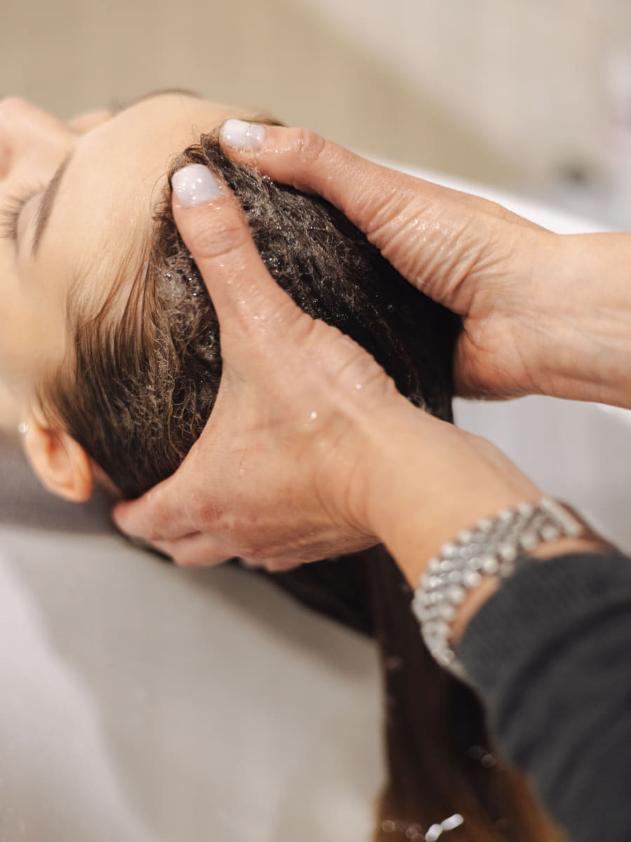 Two hands working shampoo through a client's scalp at the basin during a scalp treatment.